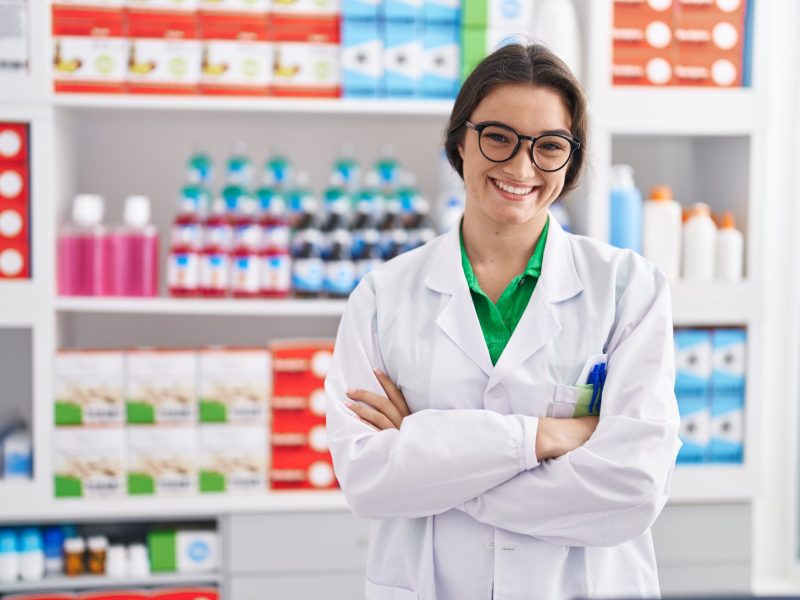 Young hispanic woman pharmacist smiling confident standing with arms crossed gesture at pharmacy
